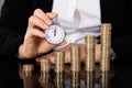 Businesswoman Holding Stopwatch In Front Of Stacked Coin