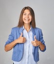 Businesswoman showing thumb up over gray background. Wearing in blue jacket. Looking at camera Royalty Free Stock Photo