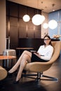 Businesswoman sitting at the airport bussiness lounge, waiting for the flight. Smiling woman wearing glasses sitting on