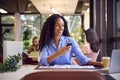 Businesswoman Sitting At Desk Approving Or Checking Proofs Or Design Layouts Using Mobile Phone