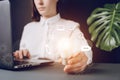 Businesswoman sitting at desk near pc on grey background, close up hand hold white light bulb with virtual icon diagram Royalty Free Stock Photo