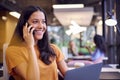 Businesswoman Sitting At Desk In Office Working On Laptop Talking On Mobile Phone Royalty Free Stock Photo