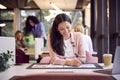 Businesswoman Sitting At Desk In Open Plan Office Approving Or Checking Proofs Or Design Layouts 