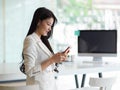 Businesswoman smiling and using smartphone while standing in office room Royalty Free Stock Photo