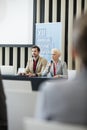 Businesswoman speaking through microphone while sitting with colleague in seminar hall Royalty Free Stock Photo