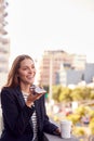 Businesswoman Standing Outside Office Building Using Mobile Phone With City Skyline In Background Royalty Free Stock Photo