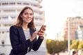 Businesswoman Standing Outside Office Building Using Mobile Phone With City Skyline In Background Royalty Free Stock Photo