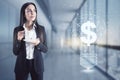 Businesswoman standing thinking in an office corridor, big windows with a cityscape, dollar sign hologram nearby. Market and price
