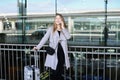 Businesswoman standing with valise and talking by smartpone near airport. Royalty Free Stock Photo