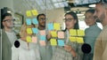 Businesswoman sticking notes on glassboard discussing ideas with colleagues clapping hands