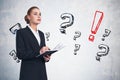 Businesswoman in suit writing in notebook, question marks sketch on grey wall