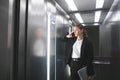 Dissatisfied businesswoman is talking on her smartphone in the elevator holding laptop in her hand. Frustrated office worker is Royalty Free Stock Photo