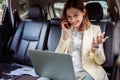 Businesswoman talking on the mobile phone and using the laptop in the car