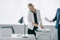 businesswoman talking on smartphone while using printer in office with colleague