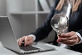 Businesswoman Typing Recent Updates On Lap Top On Desk Holding Lightbulb. Woman In Office Writing Important Message On