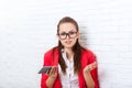 Businesswoman unsure, doubtful hold cell smart phone wear red jacket glasses stressed problem gesture