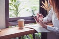 Businesswoman use mobile phone and writing a report on wood table at coffee shop near window,woking outside office lifestyle. Royalty Free Stock Photo