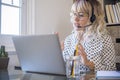 Businesswoman using laptop while talking on headphones with mic at home. Confident young woman gesturing while attending video Royalty Free Stock Photo