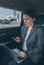 Businesswoman using mobile phone and laptop computer in car Royalty Free Stock Photo