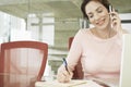 Businesswoman Using Mobile Phone While Writing On Notepad Royalty Free Stock Photo