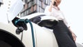 Businesswoman recharge her electric car from charging station. Peruse