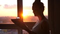 Businesswoman using tablet and looks at work papers with sunbeams and lens flare effects against sunset sky window on Royalty Free Stock Photo