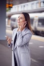 Businesswoman Waiting On Train Platform With Wireless Earbuds Answers Call On Mobile Phone