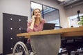 Businesswoman In Wheelchair Making Phone Call Working On Laptop In Kitchen Area Of Modern Office Royalty Free Stock Photo
