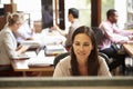 Businesswoman Working At Desk With Meeting In Background