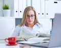 Young beauiful Caucasian businesswoman in glasses working on notebook computer and business document at office.