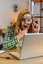 Businesswoman working at office holding magnifying glass looking at laptop screen wow expression Royalty Free Stock Photo