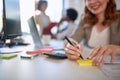 Businesswoman writing on a stickynote. Smiling woman taking notes at work