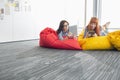 Businesswomen using digital tablets while relaxing on beanbag chairs in creative office Royalty Free Stock Photo