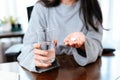 Businesswomen working at home with glass of water takes white round pill in hand