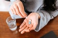 Businesswomen working at home with glass of water takes white round pill in hand