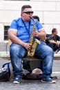 Fat busker playing sax seated on a bench