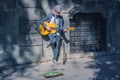 A busker street musician playing music with guitar on a city sidewalk