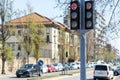 A bustling city street, lined with trees and a variety of architectural structures. A motor vehicle passes under a traffic light