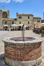 Bustling street, featuring a traditional stone well in Monteriggioni, Italy.