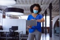 Busy african american businesswoman wearing face mask checking watch in office corridor