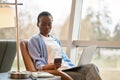 Busy African girl using mobile cell phone and laptop sitting in chair. Royalty Free Stock Photo