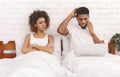 Busy african man talking on phone in bed near his furious wife