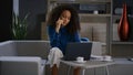 Busy african woman talking mobile phone working laptop computer in remote office Royalty Free Stock Photo