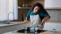 Busy arabian mom attractive curly housewife chef wears apron cooking breakfast at home kitchen stirring meal in Royalty Free Stock Photo