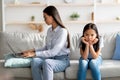 Busy asian mother working from home on laptop, sitting on sofa with daughter nearby, girl feeling neglected by her mom Royalty Free Stock Photo