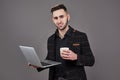 Busy bearded man in business clothes talking by smartphone and using laptop computer while holding cup of coffee in hand Royalty Free Stock Photo