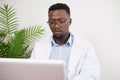 Busy Black doctor sits at his desk working on his laptop, looking serious Royalty Free Stock Photo