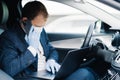 Busy businessman drives car, has phone call and checks information in laptop computer, wears disposable medical mask and gloves to