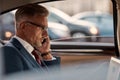 Busy businessman. Side view of mature man in classic wear sitting in the car and talking by the phone with client Royalty Free Stock Photo