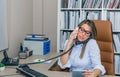 Busy businesswoman talking with cell and fixed line phone in office Royalty Free Stock Photo